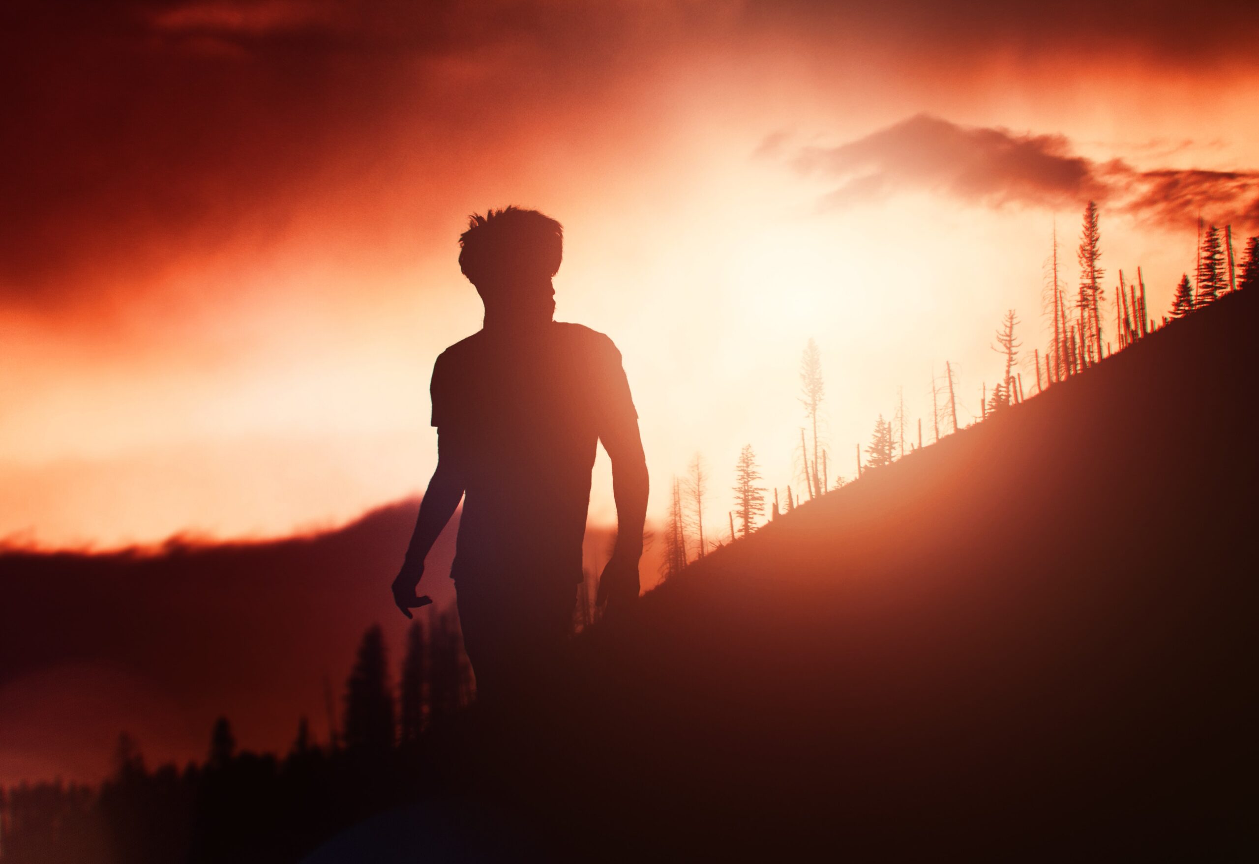 a male-presenting person outside on a steep hill silhouetted by a brilliant sun rise.